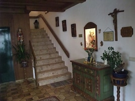 Escada que leva a um segundo andar, um armário de madeira com espelho, uma cruz e um vaso com planta.