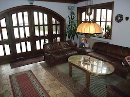 Sala de estar com sofá de couro marrom, mesa de centro de vidro e uma janela grande com luminária.