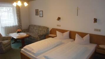 Een hotelkamer met twee eenpersoonsbedden, een sofa, een kleintje tafel met een vaas, en een kruis aan de muur.