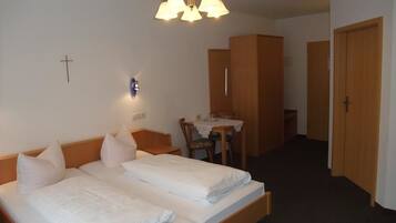 Hotellihuone, jossa on kaksi sänkyä, työpöytä, tuoli ja seinällä oleva risti.