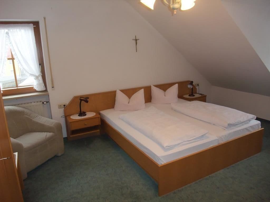 Une chambre à coucher avec un lit en bois, une table de chevet, une lampe, une chaise et une fenêtre avec des rideaux.