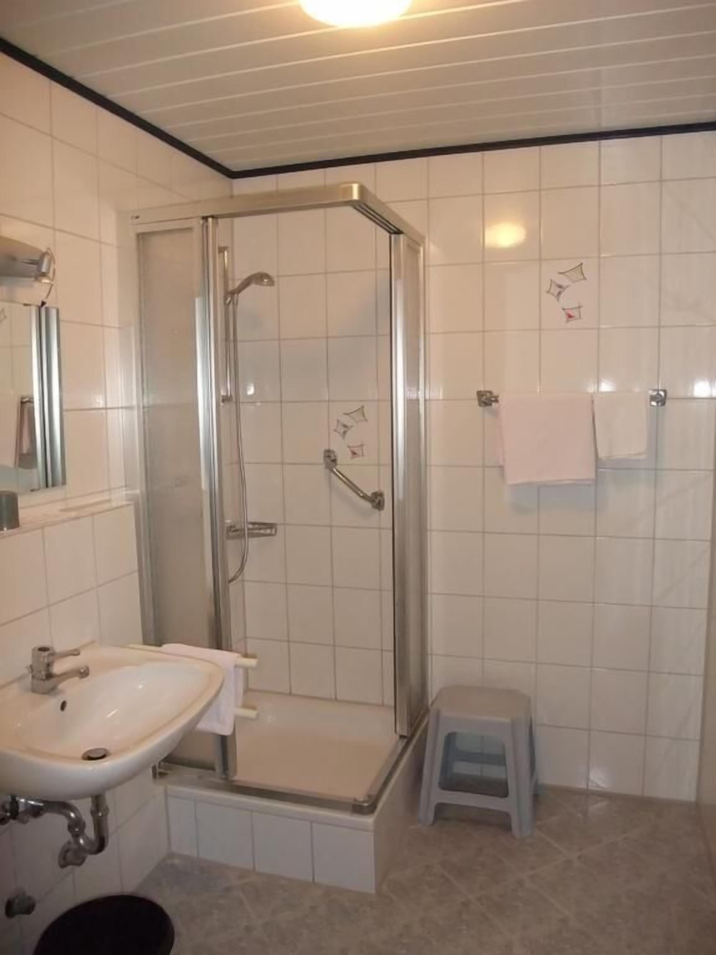 A bathroom with a glass-enclosed shower, a sink, and a small stool.