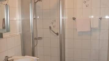 A bathroom with a glass-enclosed shower, a sink, and a small stool.