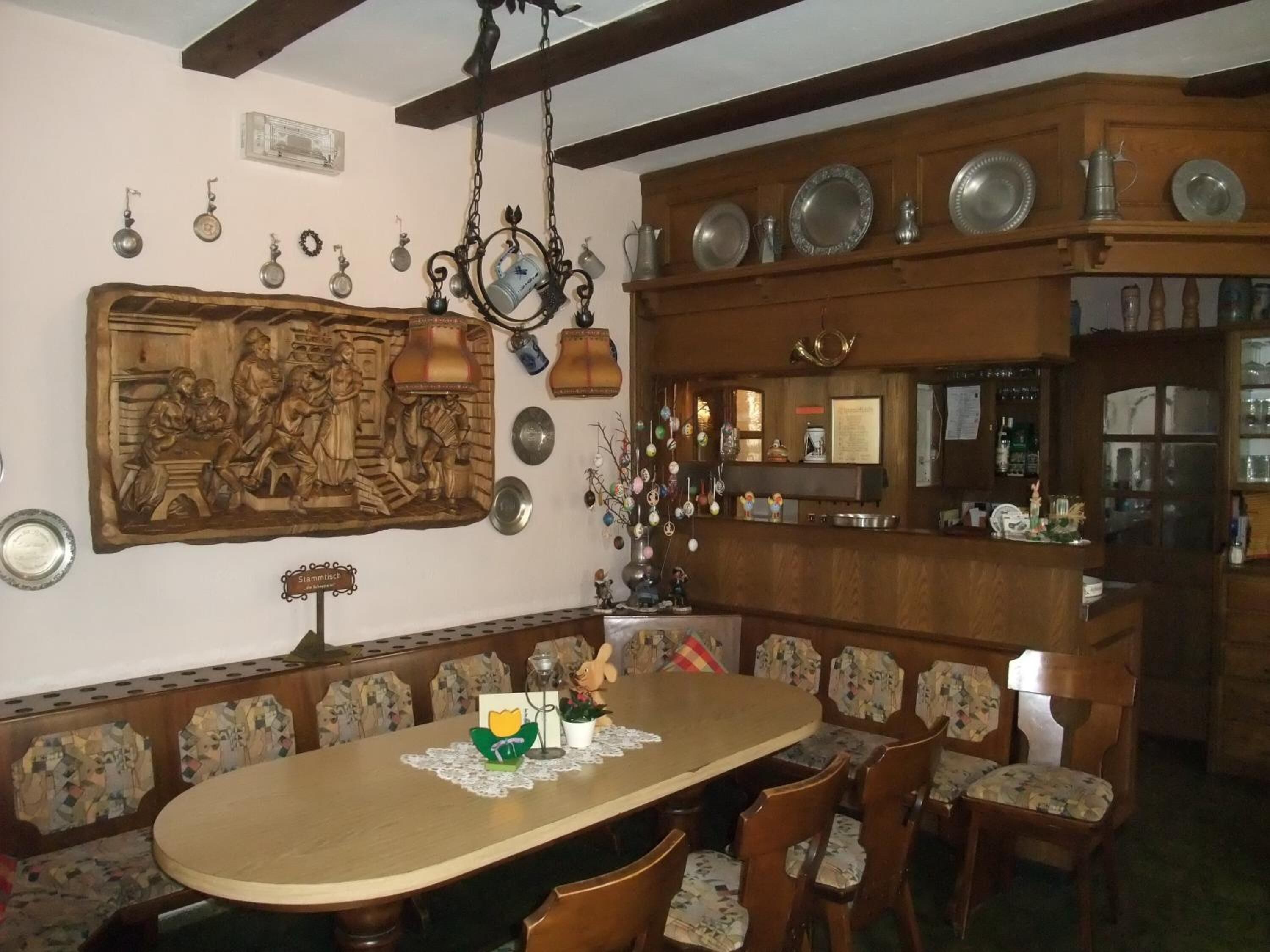 Un comedor con una mesa y sillas de madera, un panel de madera tallada en la pared, y una zona de bar con estantes llenos de platos y botellas.