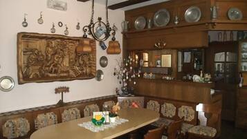 Un comedor con una mesa y sillas de madera, un panel de madera tallada en la pared, y una zona de bar con estantes llenos de platos y botellas.