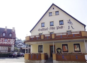 A building with a sign reading "Gästhof Alte Post". It has a balcony with wooden railings and flower boxes.