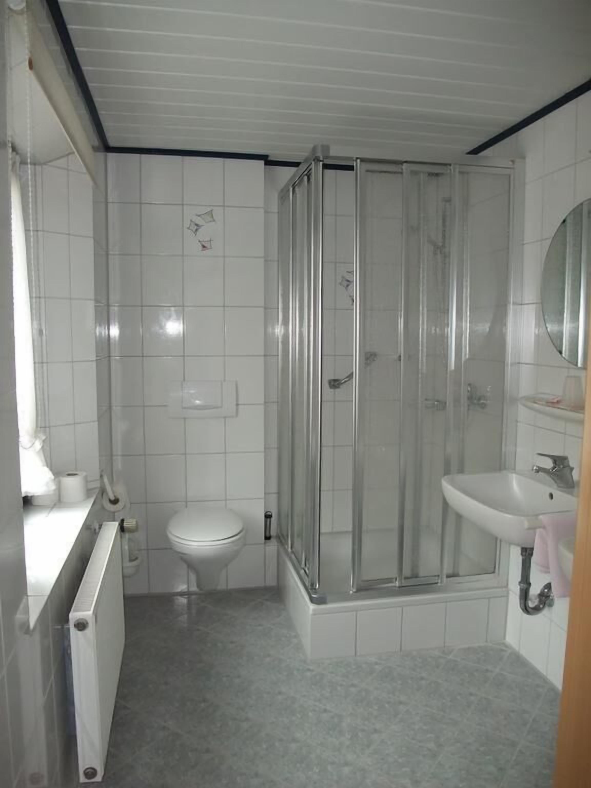 A bathroom with a shower enclosure, toilet, and sink.