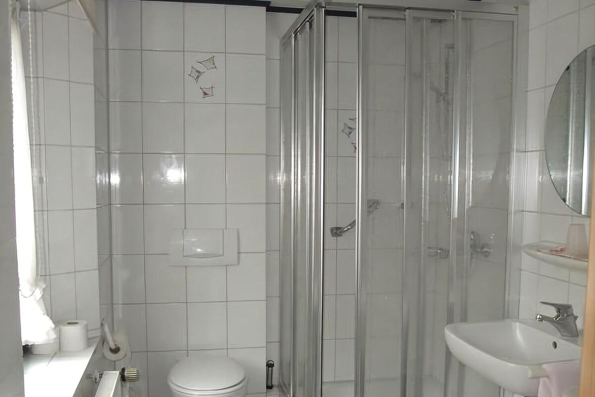 A bathroom with a glass-enclosed shower, a toilet, and a sink with a mirror.