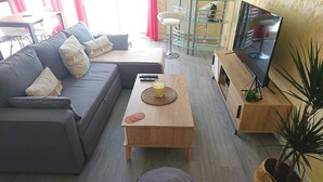 A modern living room with a grey sofa, a wooden coffee table, and a TV stand with a flat-screen TV. - Large apartment T2, quiet, near Lyon, balcony parking and transport (Saint-Priest)
