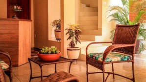 A reception area with a wooden desk, wicker chairs, potted plants, and a staircase. - Pousada Casa Grande (Barra do Garcas)