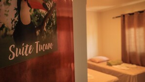 A hotel room with a bed, a small table, and a sign reading "Suite Tucano". - Pousada Casa Grande (Barra do Garcas)