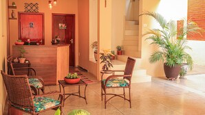 A reception area with a wooden desk, two wicker chairs, and potted plants. - Pousada Casa Grande (Barra do Garcas)