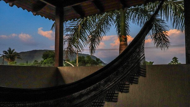 A hammock under a roofed area with a view of palm trees and a mountain in the background. - Pousada Casa Grande (Barra do Garcas)
