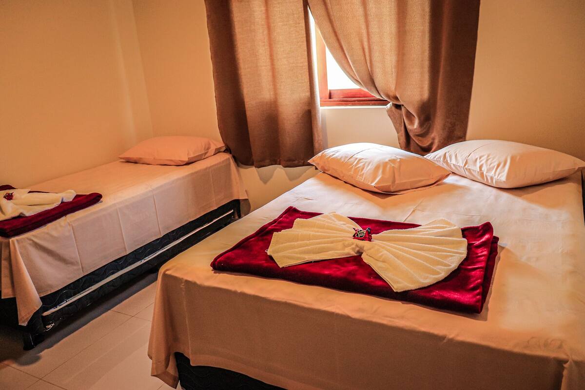 A hotel room with two single beds, each with a pillow and a blanket.