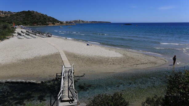 A beach with clear water, a wooden walkway, and a person walking. - Blu Acqua (Agios Nikolaos)