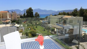 A balcony with a glass railing overlooking a pool and a mountainous landscape. - Blu Acqua (Agios Nikolaos)