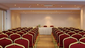 A conference room with rows of red chairs and a white table at the front. - Blu Acqua (Agios Nikolaos)
