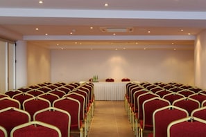 A conference room with rows of red chairs and a white table at the front. - Blu Acqua (Agios Nikolaos)
