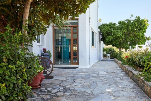A stone-paved pathway leading to a white building with a glass door and windows. - Blu Acqua (Agios Nikolaos)