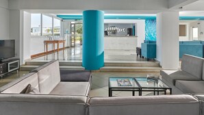 A modern hotel lobby with a large blue pillar, comfortable seating, a reception desk, and a view of the outside. - Blu Acqua (Agios Nikolaos)