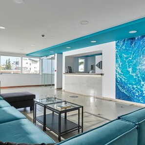 A modern hotel lobby with a reception desk, seating area, and a large window providing a view of the outside. - Blu Acqua (Agios Nikolaos)