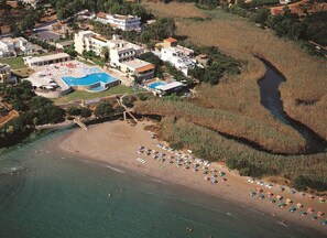 An aerial view of a coastal resort with a swimming pool, beach, and several buildings. - Blu Acqua (Agios Nikolaos)