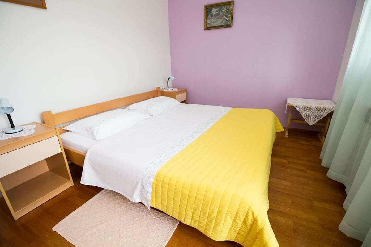A bedroom with a bed, bedside table, lamp, and a small table with a lace tablecloth.