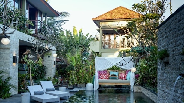 A serene pool area with lounge chairs, a bed with a canopy, and lush tropical plants. - Lin Ubud (Ubud)