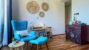 A room with a blue armchair, a small round table, a wooden cabinet, and a wall with woven decorations. - Lin Ubud (Ubud)
