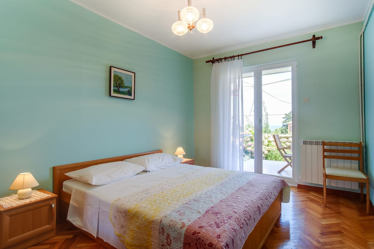 A bedroom with a bed, bedside lamps, a picture on the wall, and a view of the outdoors through a window.