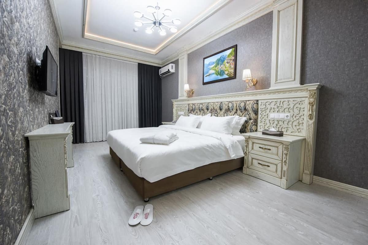 Quarto de hotel moderno com cama grande, mesa de cabeceira, televisão e cabeceira decorativa.