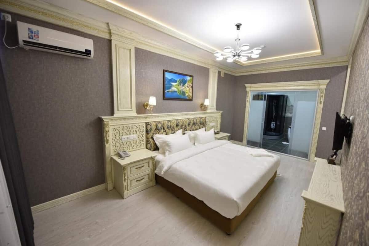 Quarto com uma cama grande, uma mesinha de cabeceira, ar-condicionado fixado na parede, luminária de teto e um quadro emoldurado.
