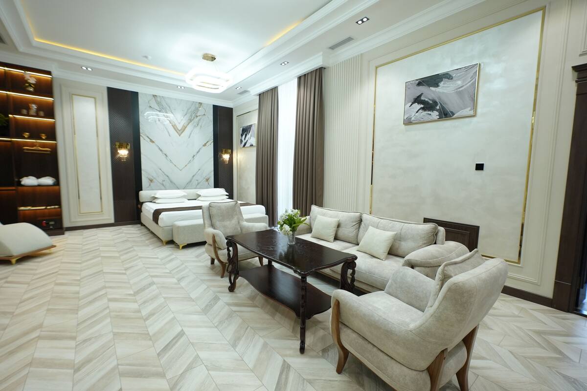 Uma sala de estar ampla com piso em padrão herringbone, uma mesa de centro de madeira escura e um conjunto de sofá bege.