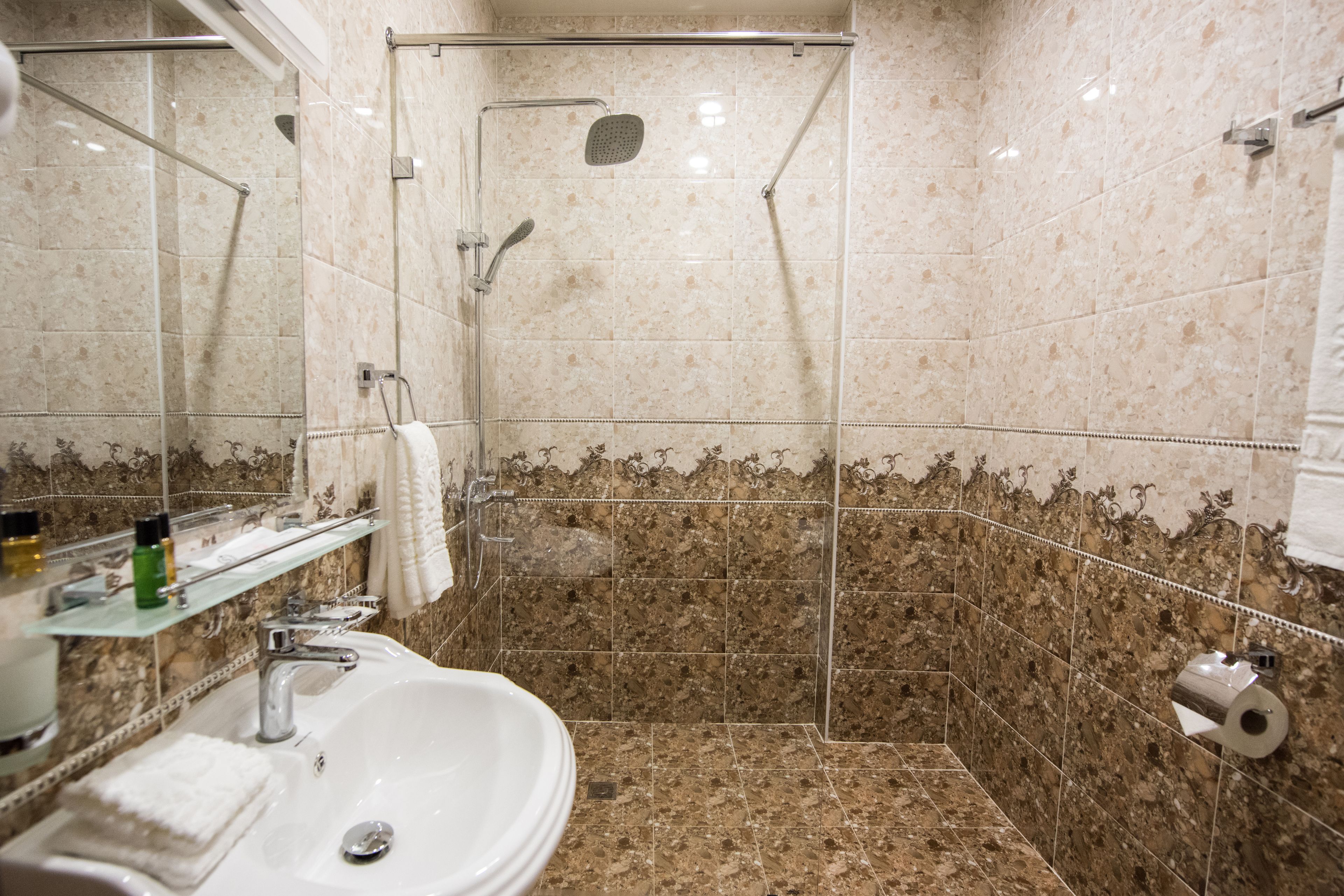 A bathroom with a sink, mirror, shower, and marble tiles.