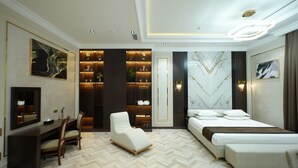 A modern bedroom with a bed, bedside tables, a seating area, and a built-in shelving unit. - Simma Hotel spa and waterpark (Tashkent)