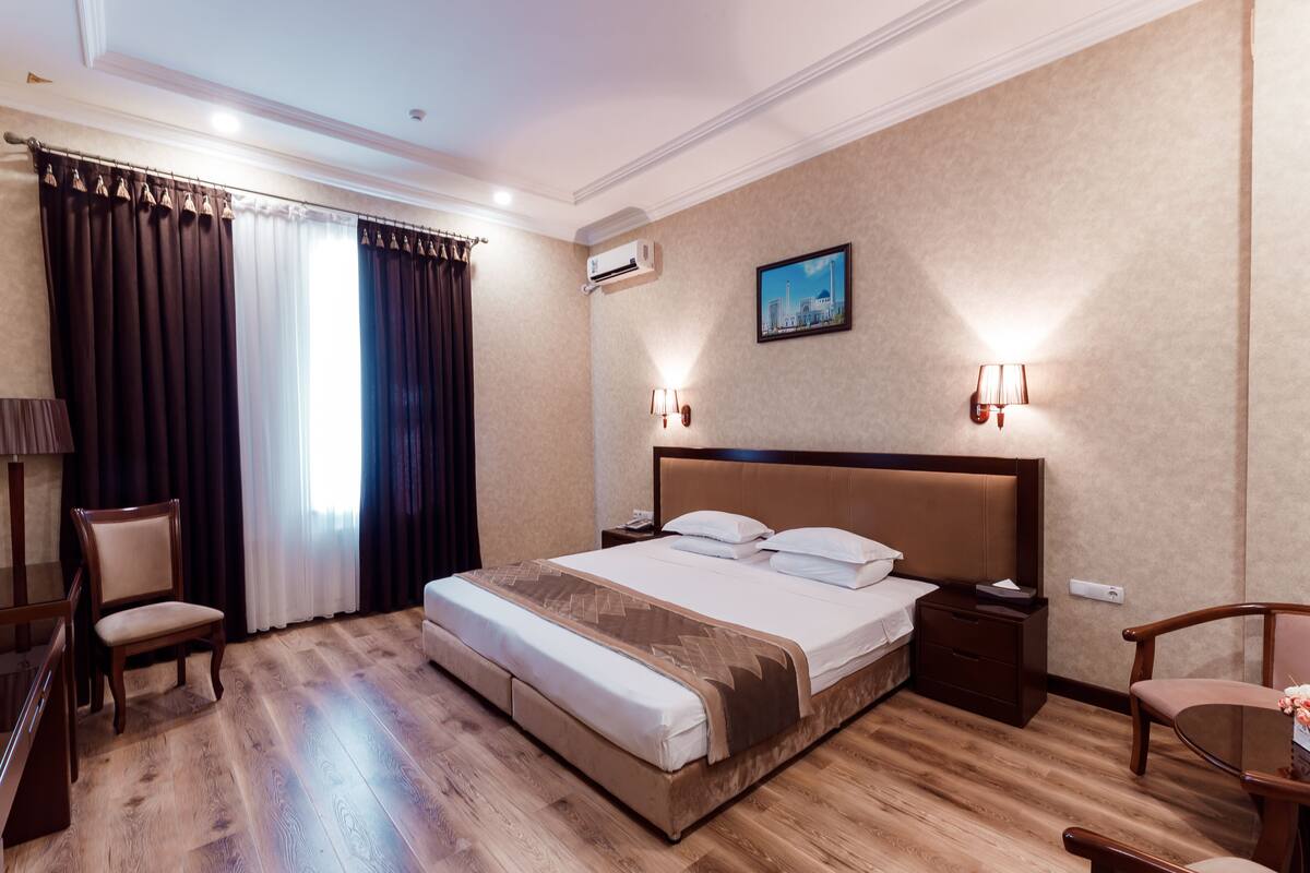 Quarto de hotel com uma cama grande, piso de madeira, escrivaninha e uma cadeira.