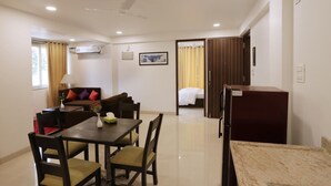 A hotel room with a dining area, a bed, a ceiling fan, and a refrigerator. - Goa Junction Vagator - Apparthotel (Vagator)