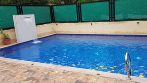 A swimming pool with a clear blue water surface, a tiled deck, and a metal ladder. - Goa Junction Vagator - Apparthotel (Vagator)