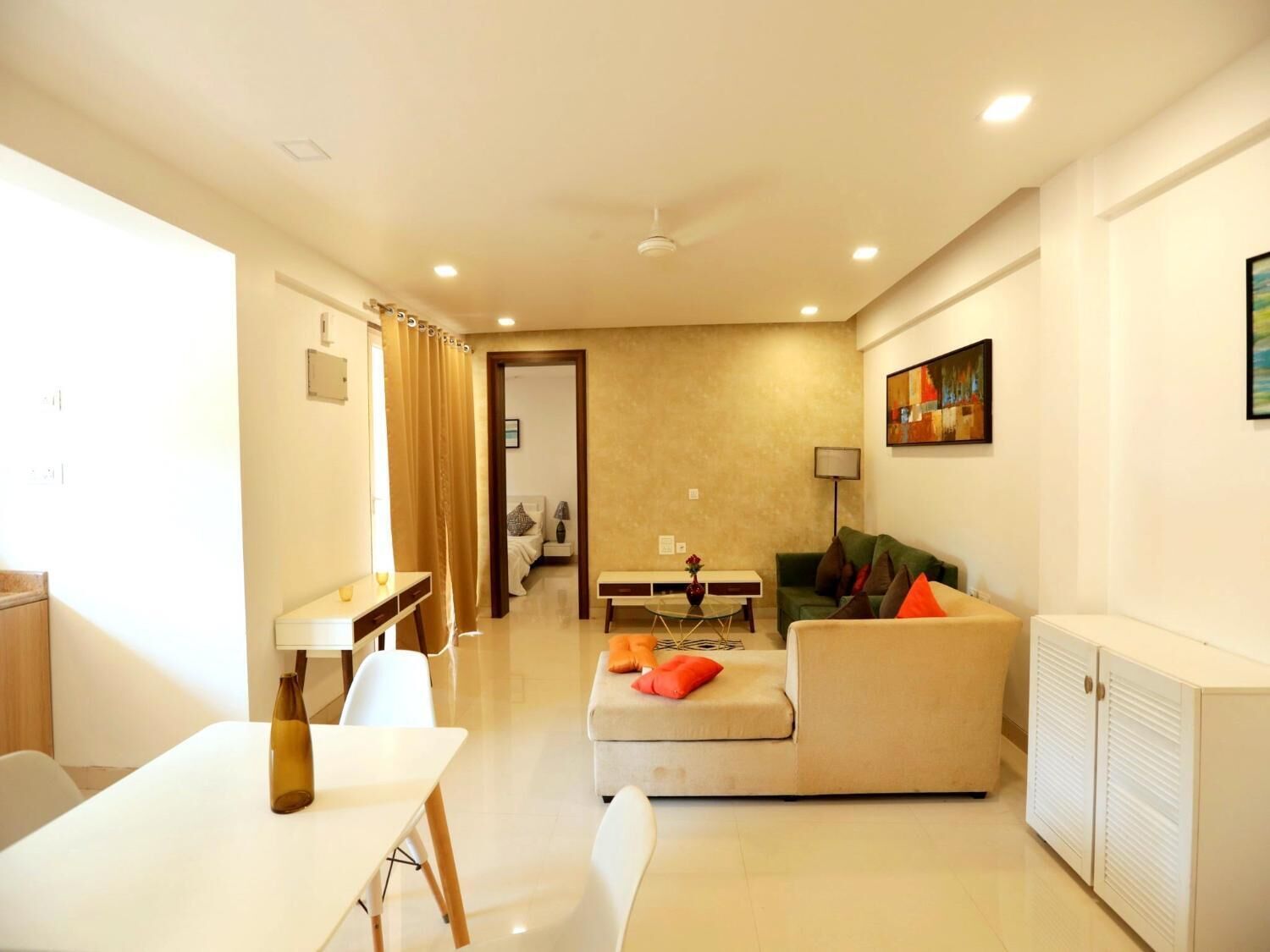 A modern living room with a sofa, a dining table, and a kitchen area visible through an open door. - Goa Junction Vagator - Apparthotel (Vagator)