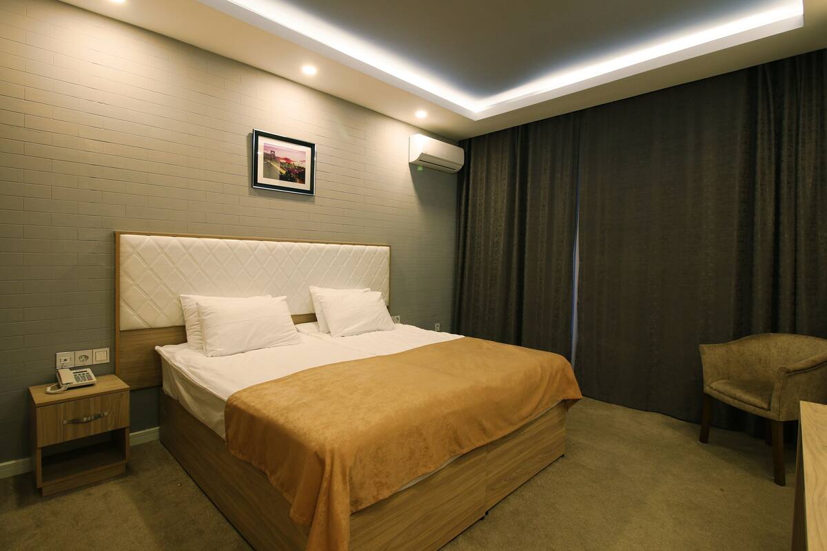 A hotel room with a large bed, a nightstand with a phone, a chair, and a picture on the wall.