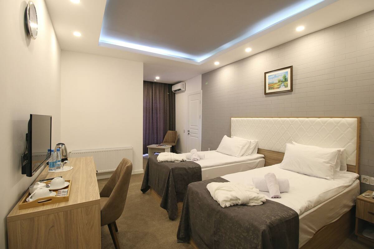 A hotel room with two beds, a desk with a chair, a TV, and a painting on the wall.