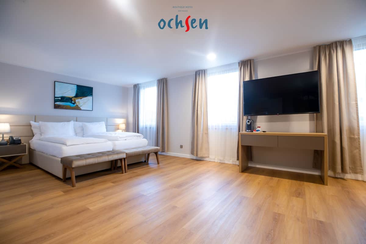 A hotel room with a bed, a desk, a TV, and a painting on the wall.