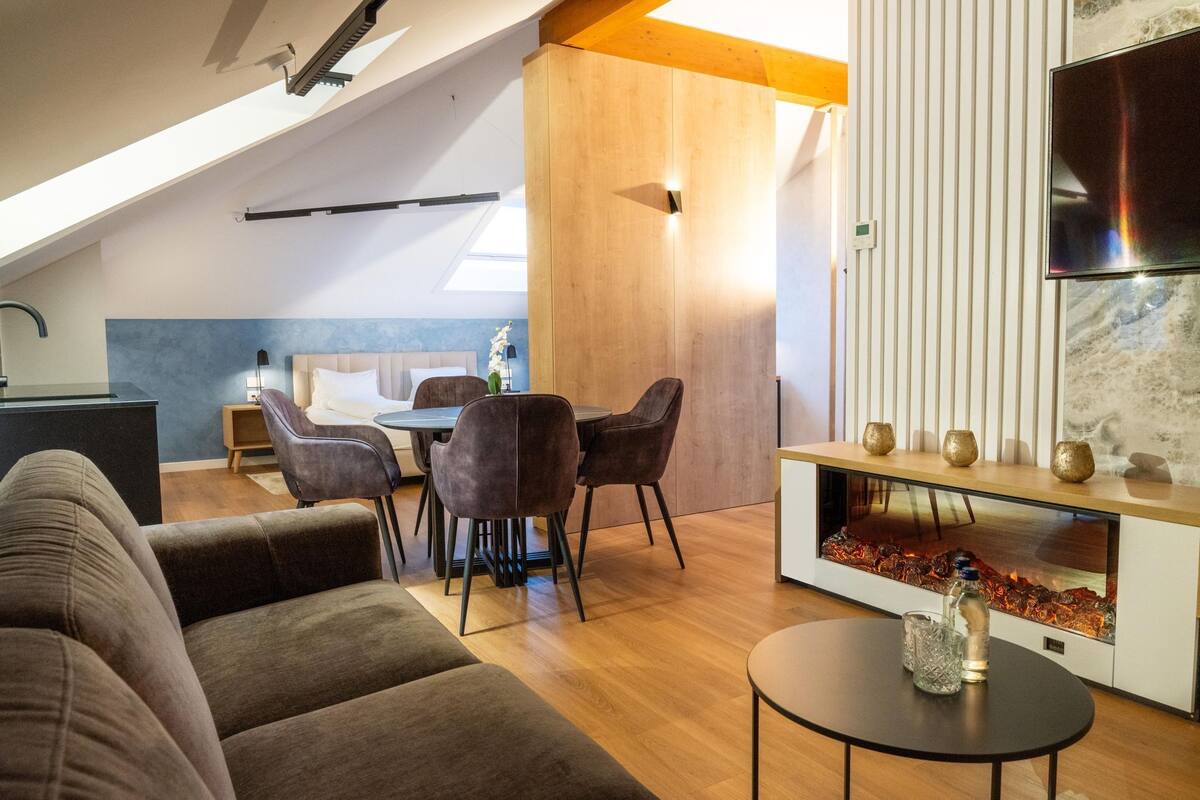A modern living room with a fireplace, a dining area, and a TV mounted on the wall.