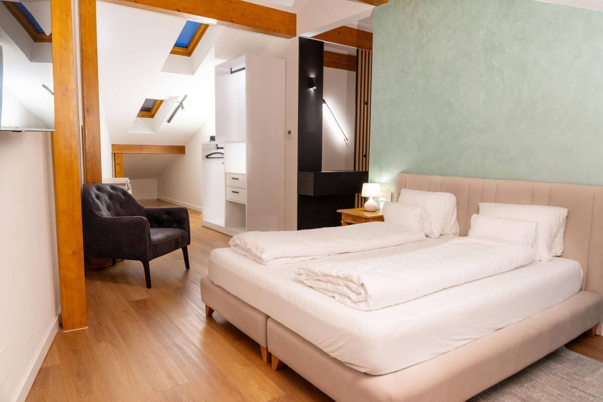 A bedroom with a large bed, a chair, a desk, and a wardrobe.