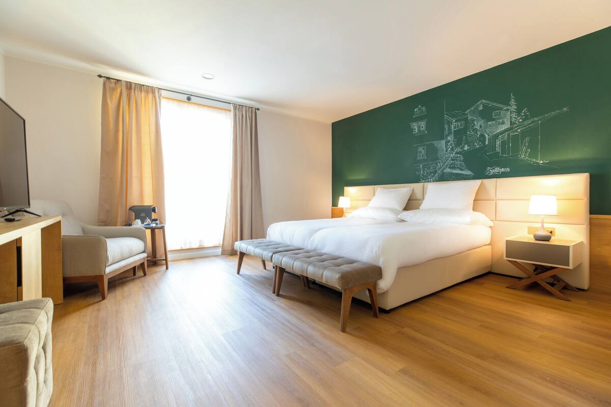 A modern hotel room with a large bed, a desk, a chair, and a view of a town.