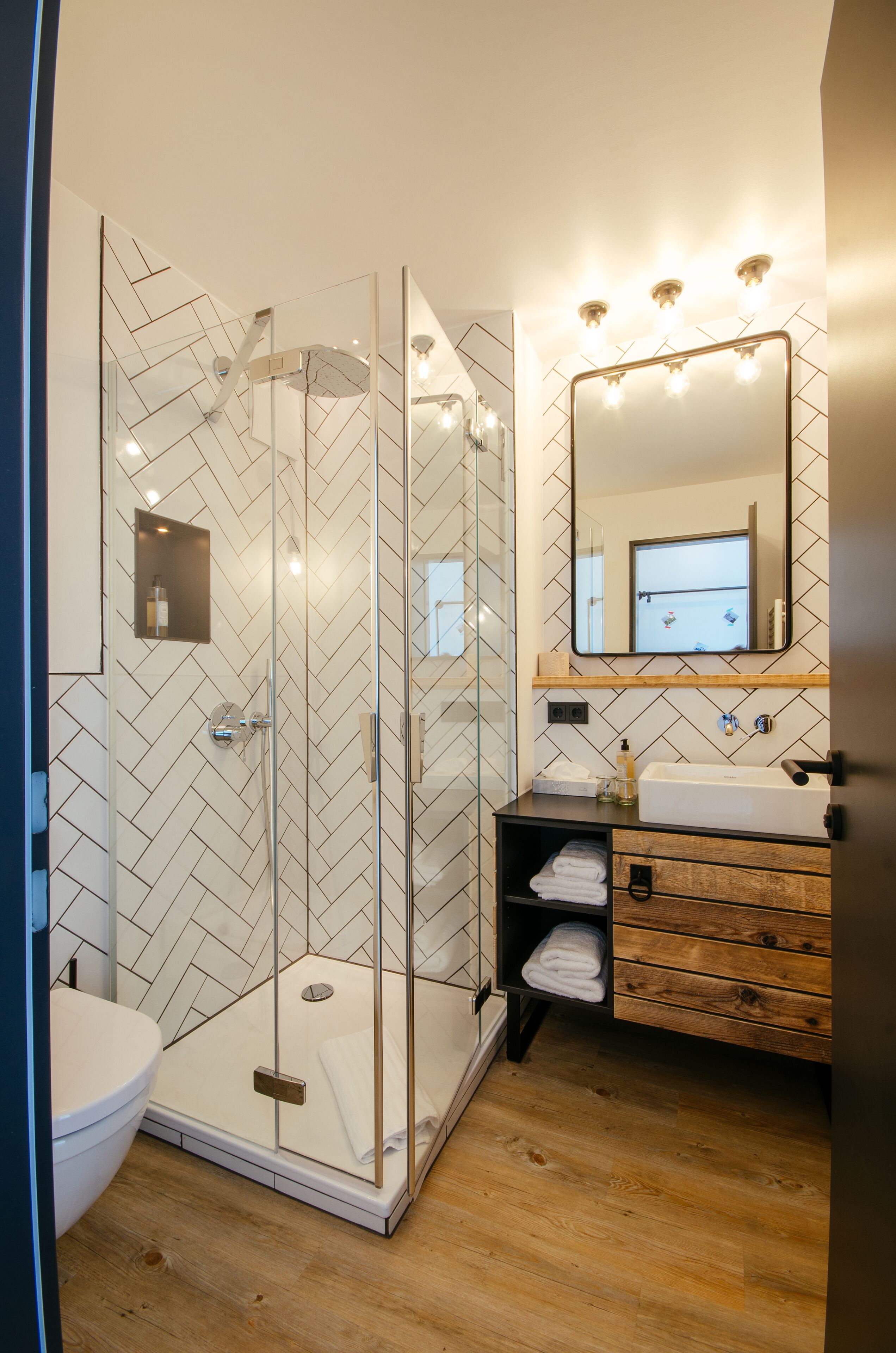 A modern bathroom with a glass-enclosed shower, a wooden vanity, and a large mirror above the sink.