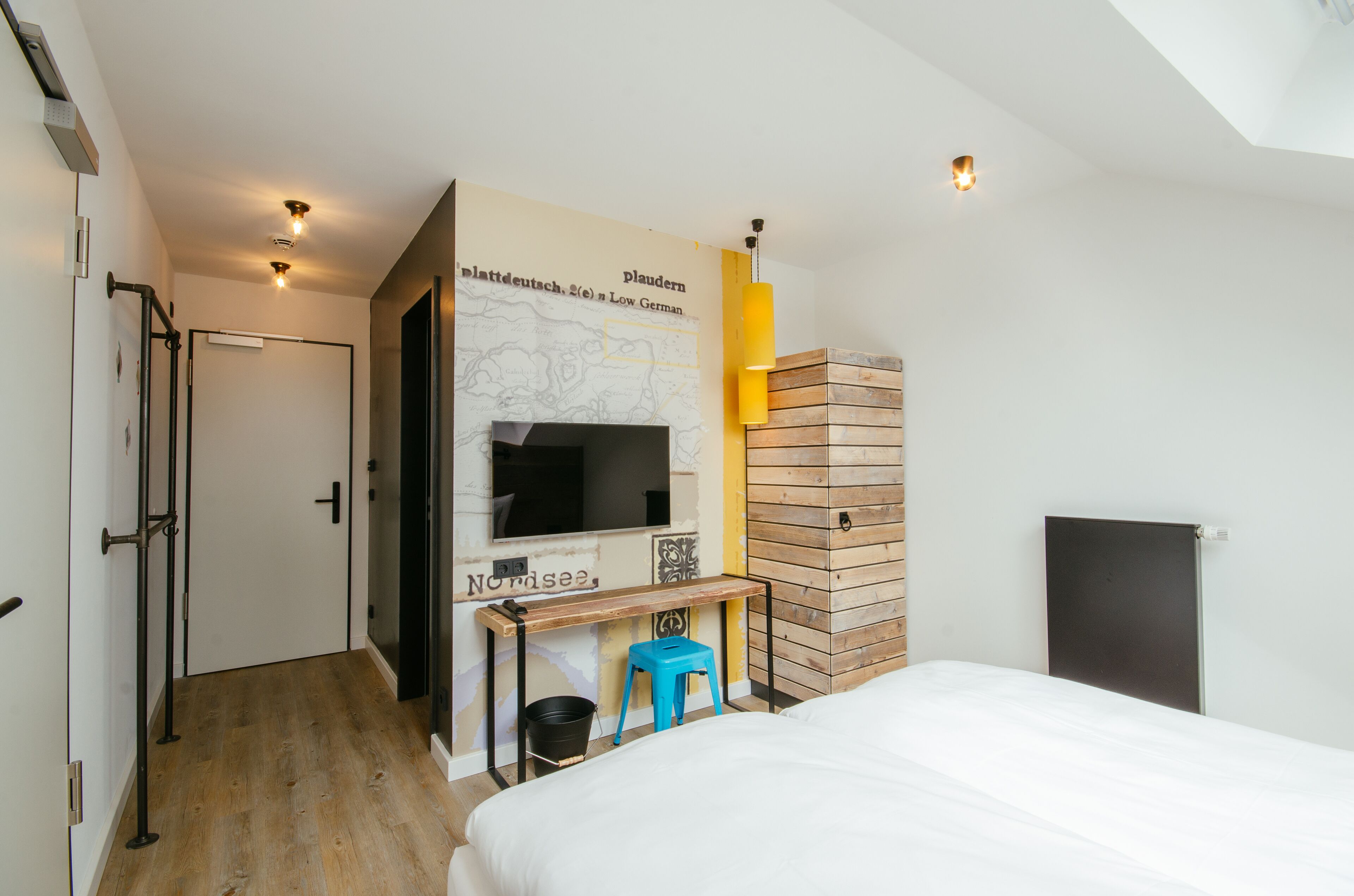 Une chambre d’hôtel moderne équipée d’un lit, d’un bureau avec un ordinateur, d’une carte accrochée au mur et d’un mur recouvert de panneaux en bois.