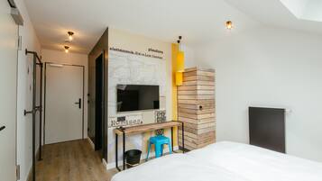 Une chambre d’hôtel moderne équipée d’un lit, d’un bureau avec un ordinateur, d’une carte accrochée au mur et d’un mur recouvert de panneaux en bois.