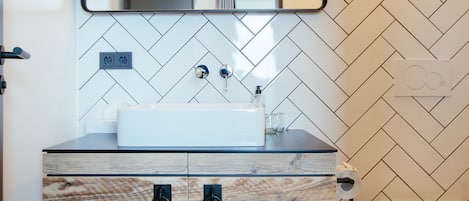 Un baño con pared de blanco diseño espiga, tocador de madera con cajones, espejo y un inodoro.