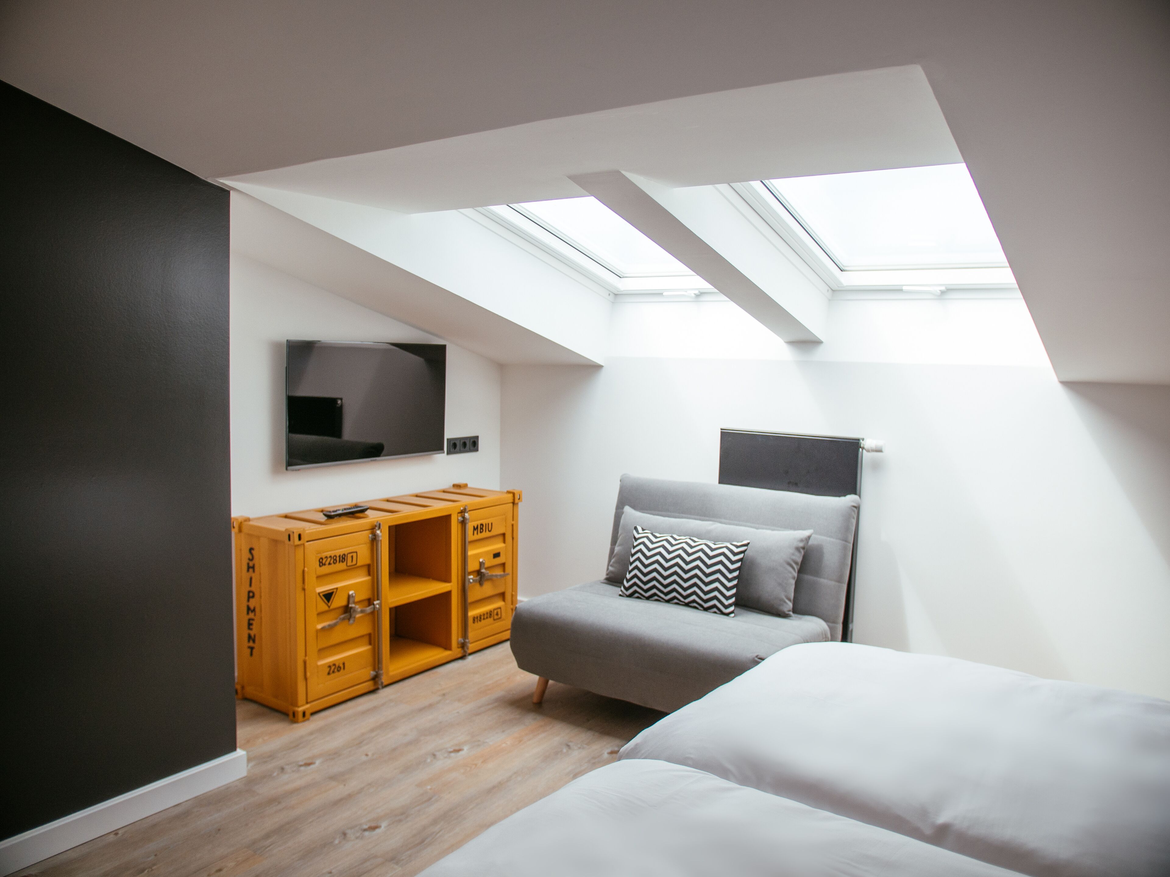 Un dormitorio moderno con tragaluces, una cama, un sofá y un mueble de almacenamiento de madera.